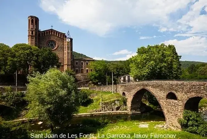 puente sobre el rio, en pueblo sant joan de les fonts de comarca la garrotxa, vistas de pueblo e iglesia y hay arboles verdes